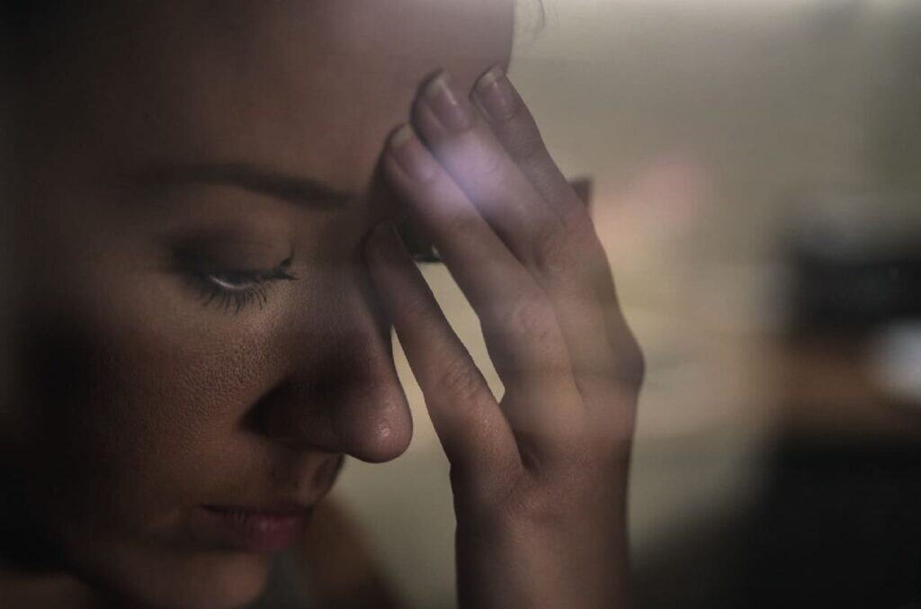 Una mujer con los ojos cerrados apoya la mano en la frente, parece estresada o sumida en sus pensamientos.