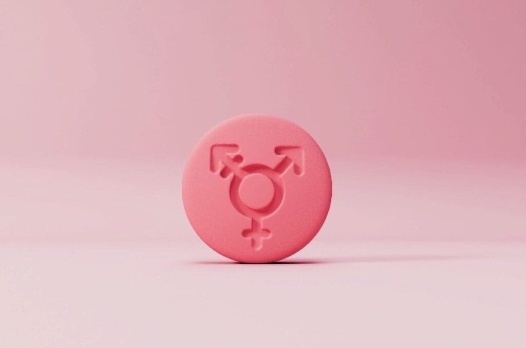 Un objeto redondo de color rosa presenta un símbolo transgénero en relieve, sobre un fondo rosa.